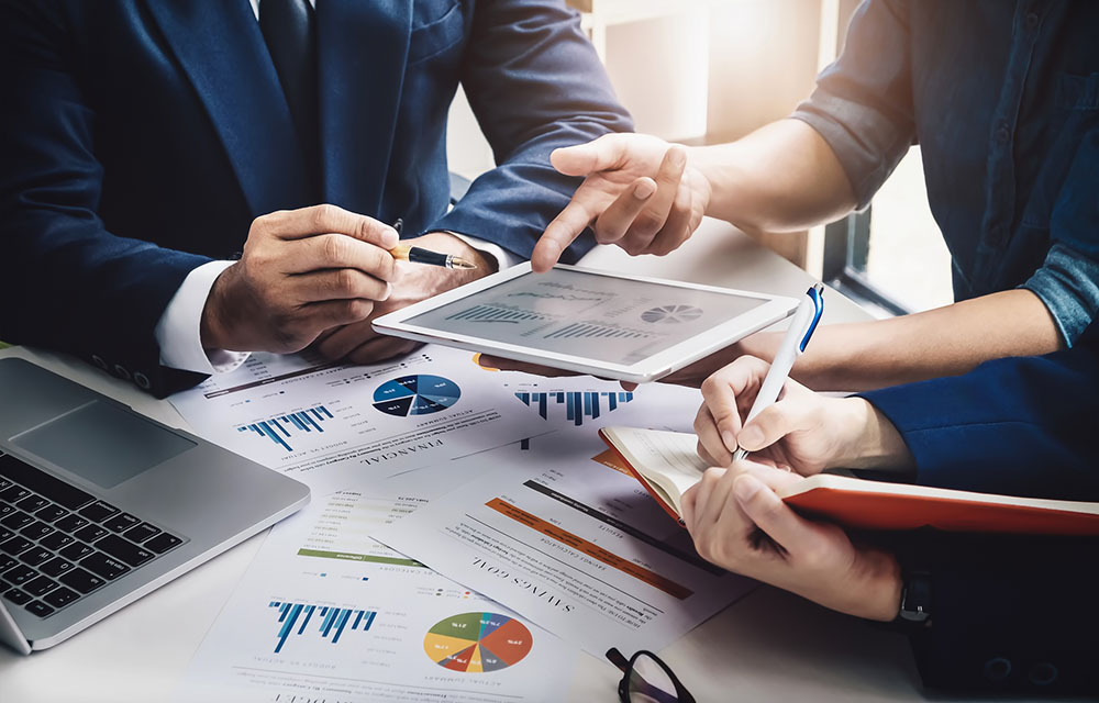 Team of economists deliberating on an assortment of charts spread across the table.