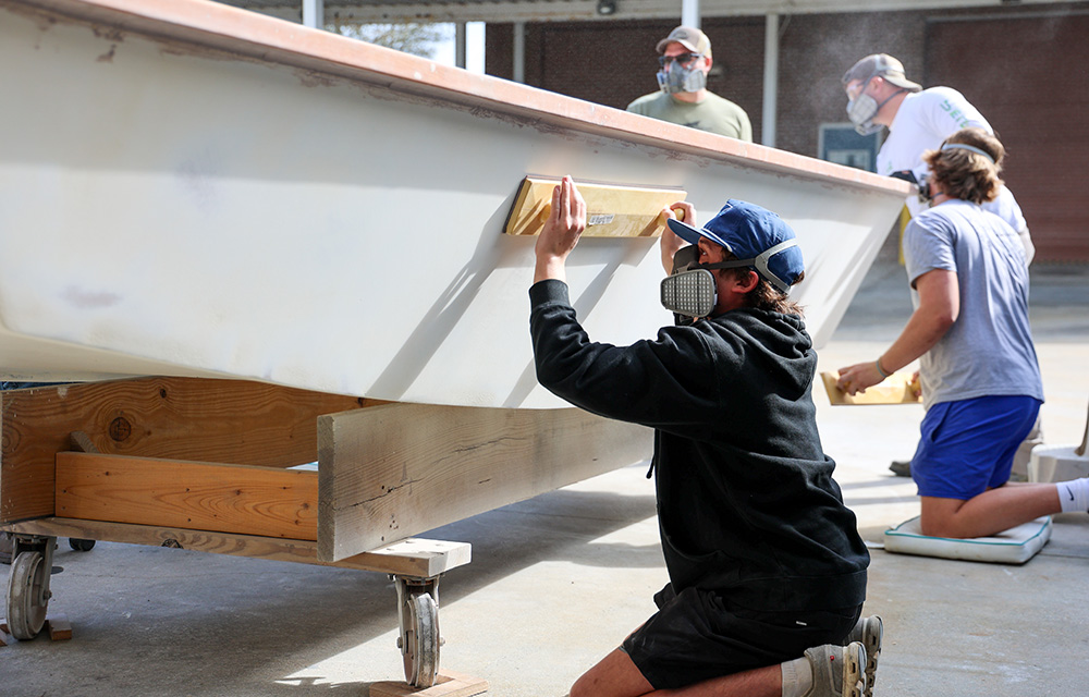 Community college students wearing protective masks as they sand down a boat.