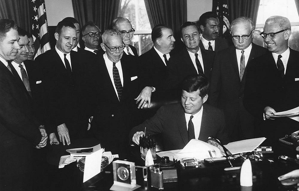 John F Kennedy signing bill with his colleagues standing around him