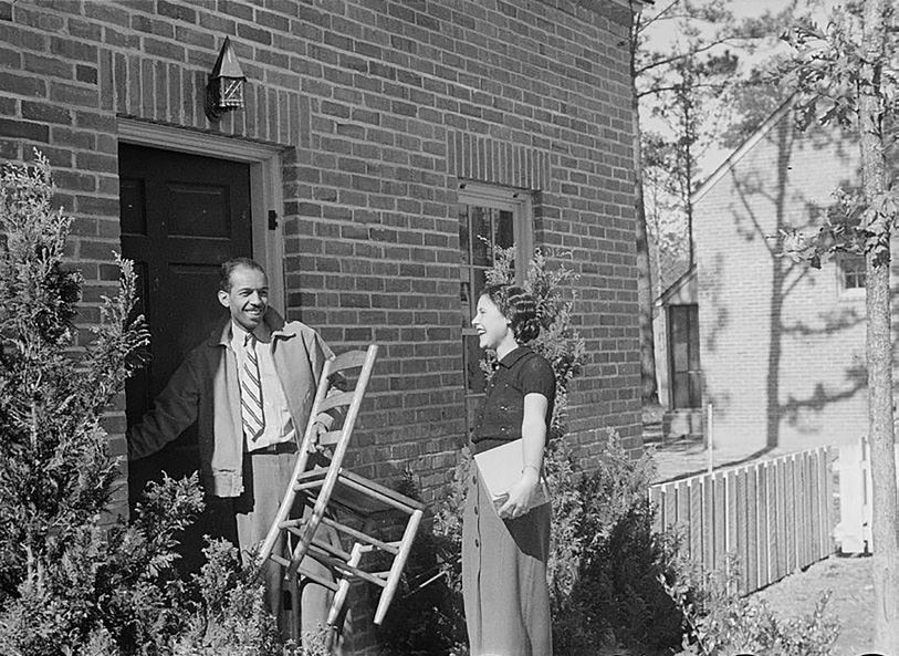 A couple moving into a house with the man carrying a chair through the door.