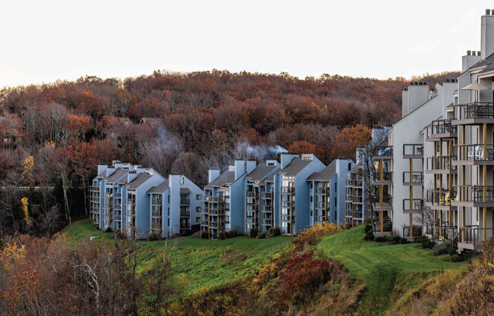 Apartment buildings lined across a hill in a rural area with Fall colored trees surrounding.