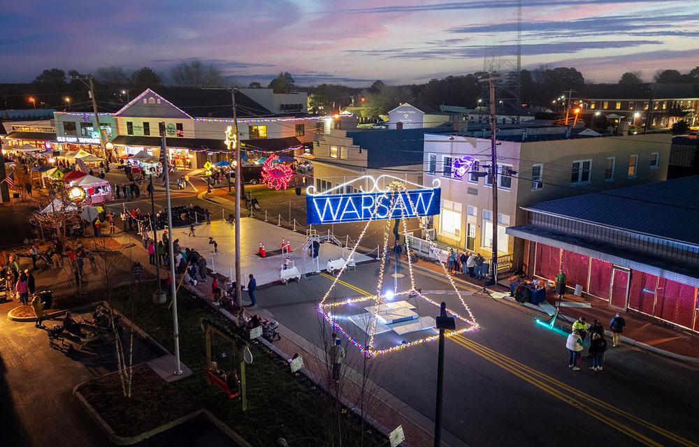A festival with lights and concession stands being held in downtown Warsaw, Virginia at dusk.