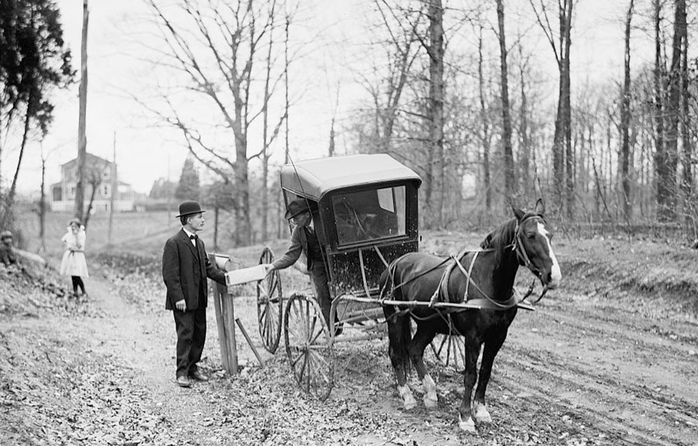 A rural free delivery mail carrier making a delivery with their horse-drawn postal delivery wagon.