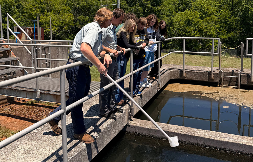 Pre-apprentices at a water treatment plant observing their instructor as he collects a water sample.
