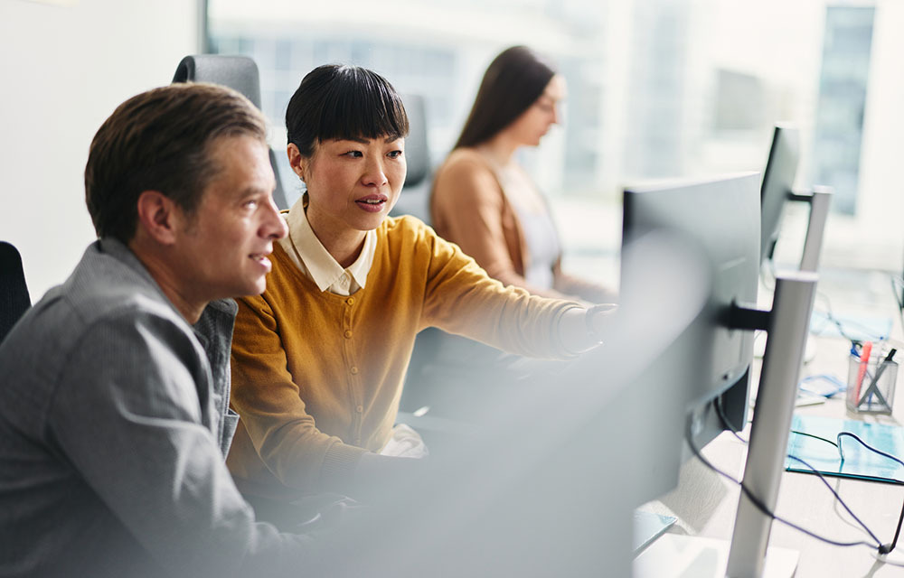 Employee pointing out a date on her computer to her coworker.