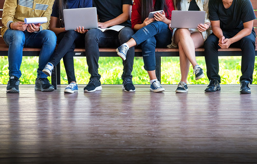 Students sitting on a bench with laptops and notebooks in hand