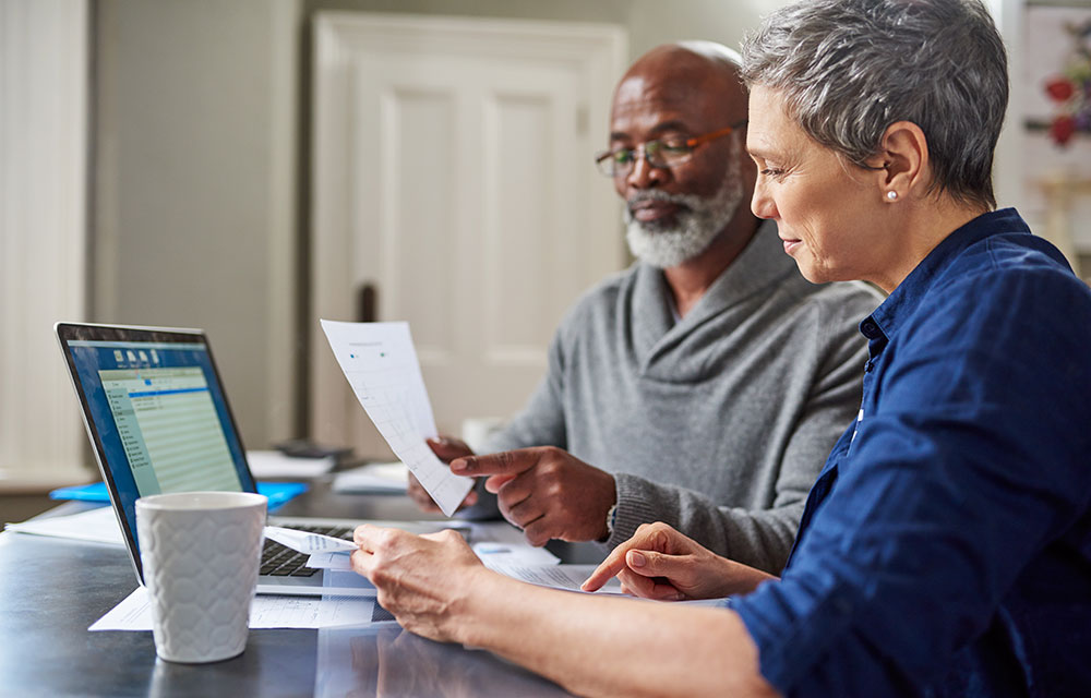 Two older workers sitting in front of laptop while looking at documents.