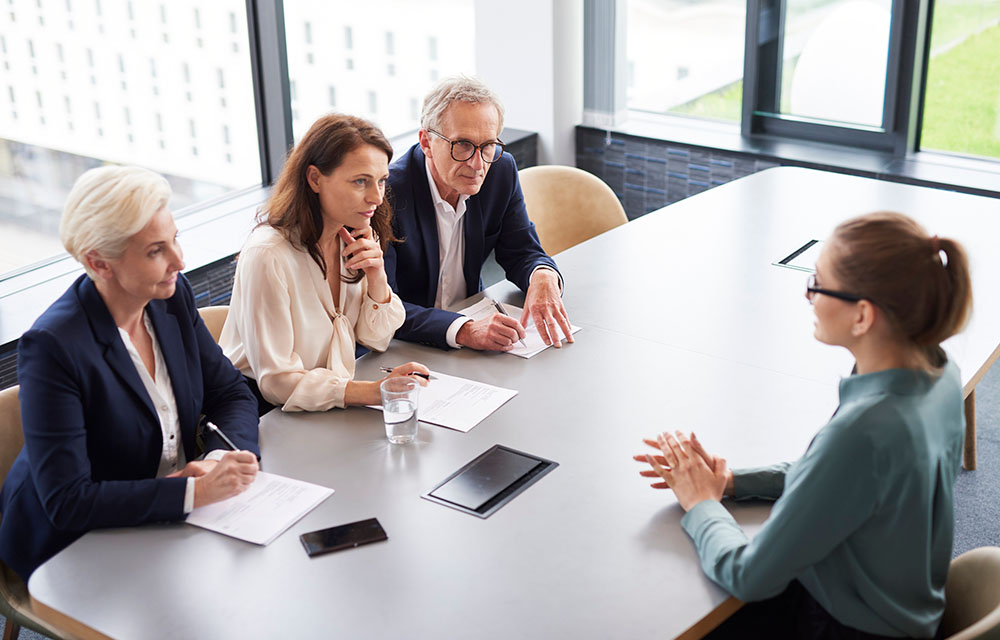 Three professionals sit across a table from an interviewee.