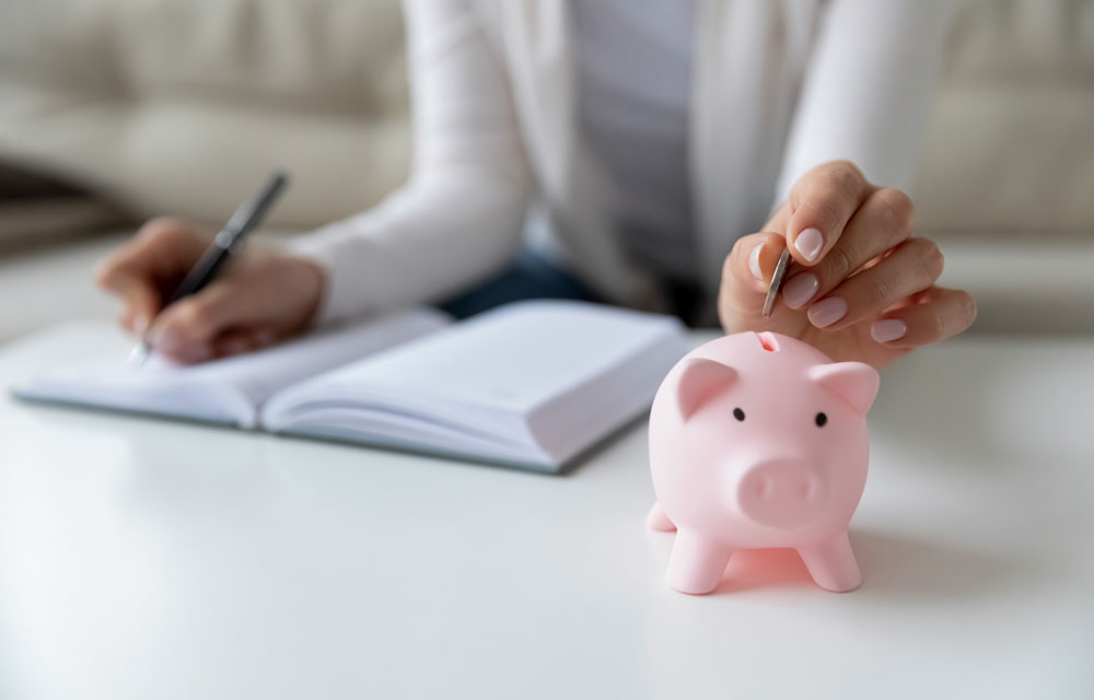 making notes in a book next to a piggy bank