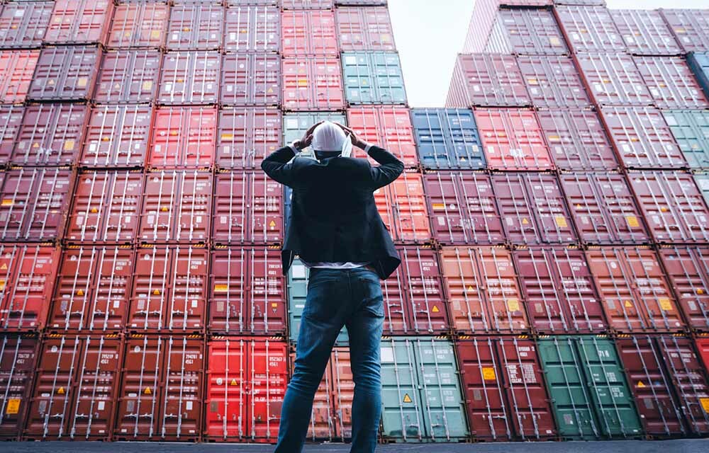  a worker outside a large pile of shipping containers