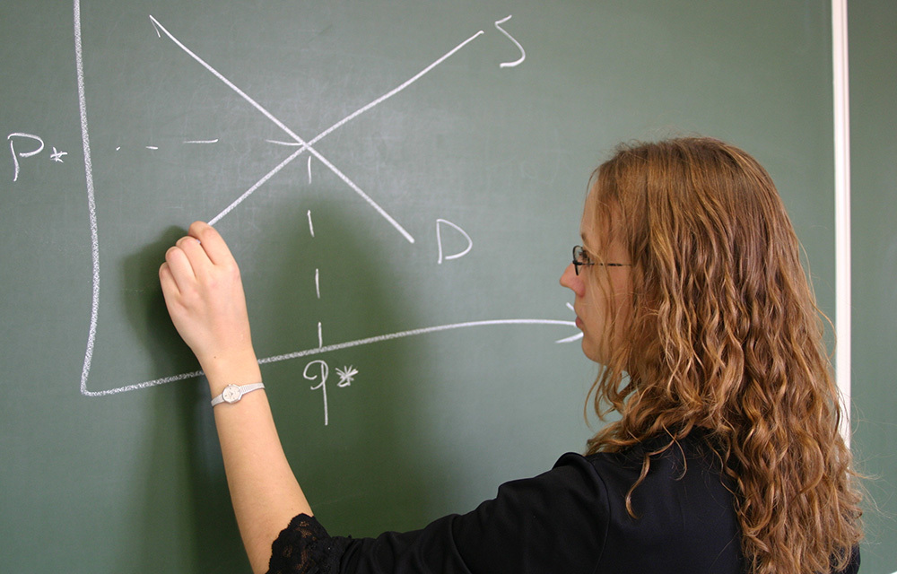 redhead teacher drawing supply and demand curves on the blackboard