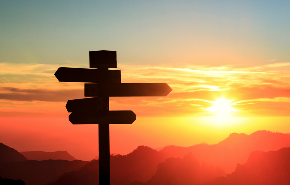 Directional sign silhouetted against the sunset.