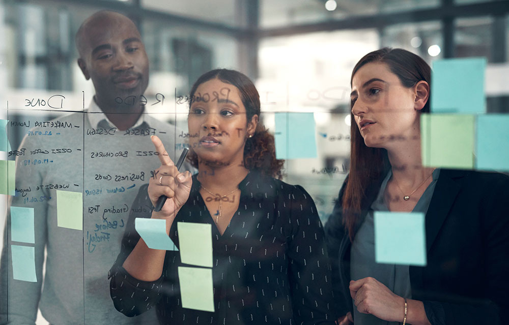 two women and one man discussing business on a glass wall with sticky notes