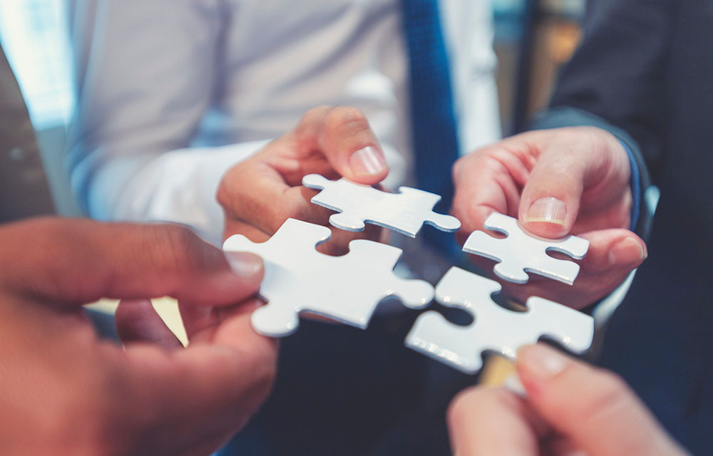 Four people holding small puzzle pieces together