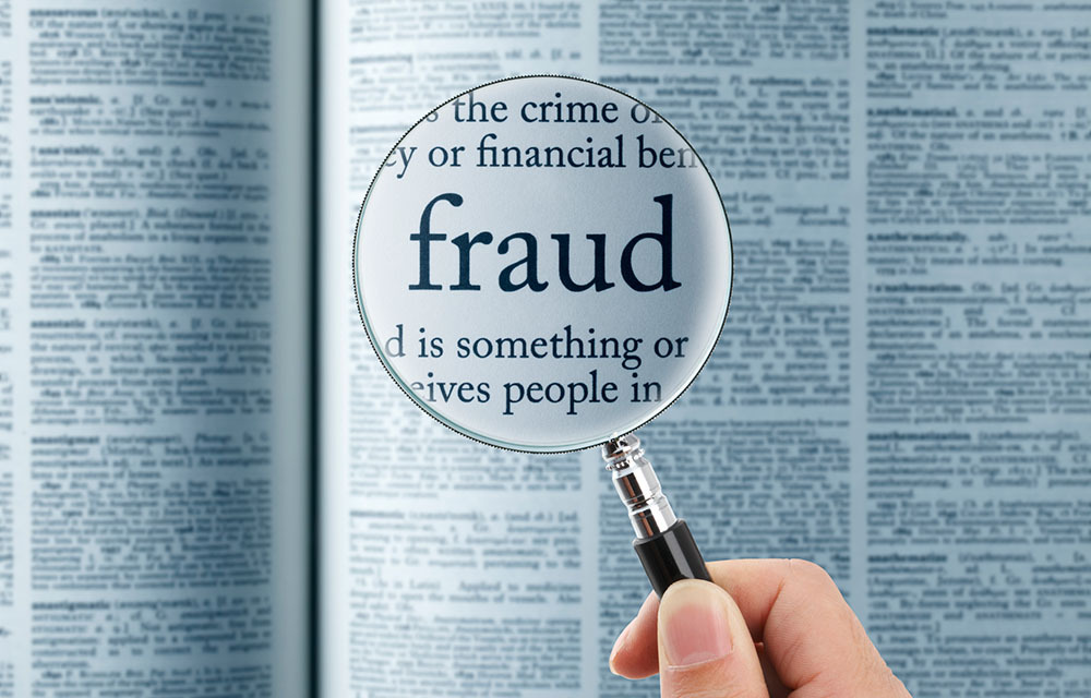 Person holds a magnifying glass over the word "fraud" in a book