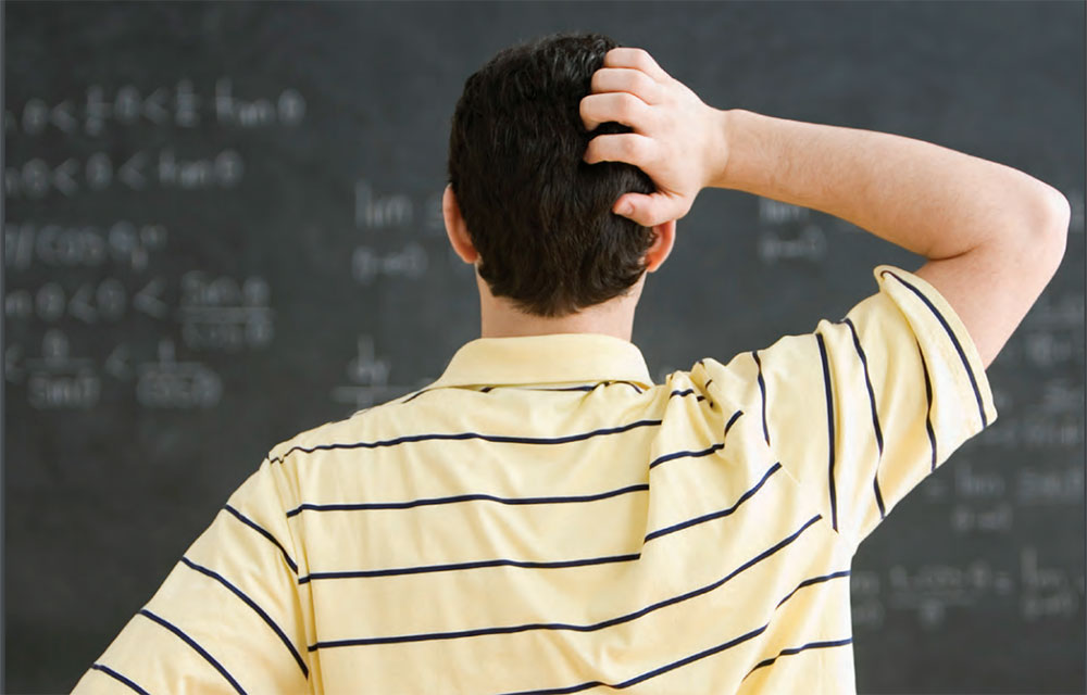 man scratches his head at a blackboard formula