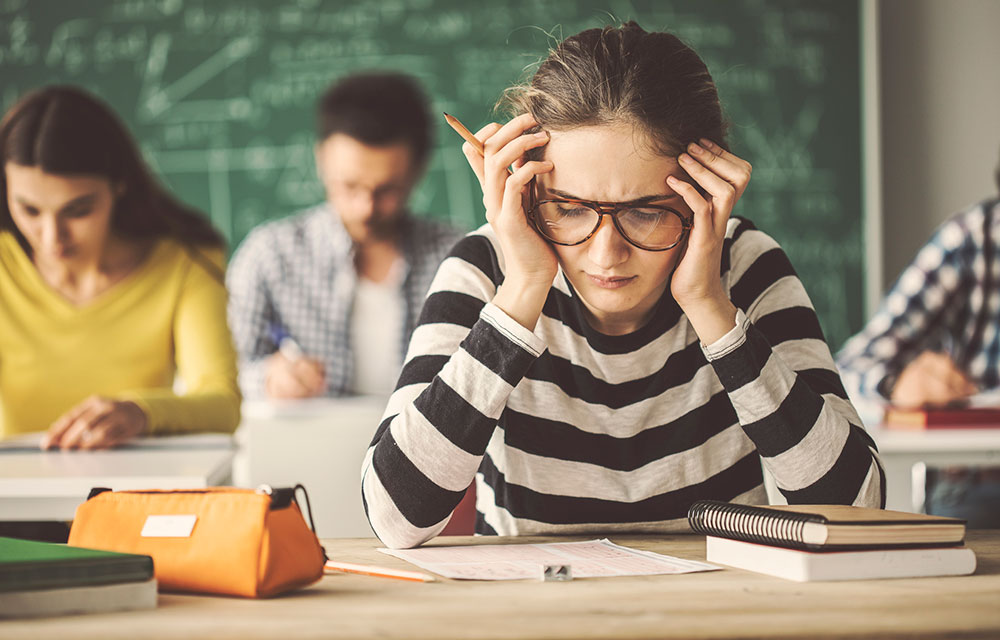 college students taking a test and a woman in the foreground stressed