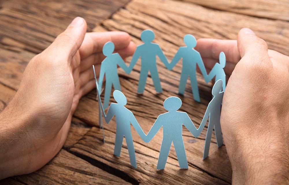 Paper dolls holding hands in a circle, cupped by a pair of human hands