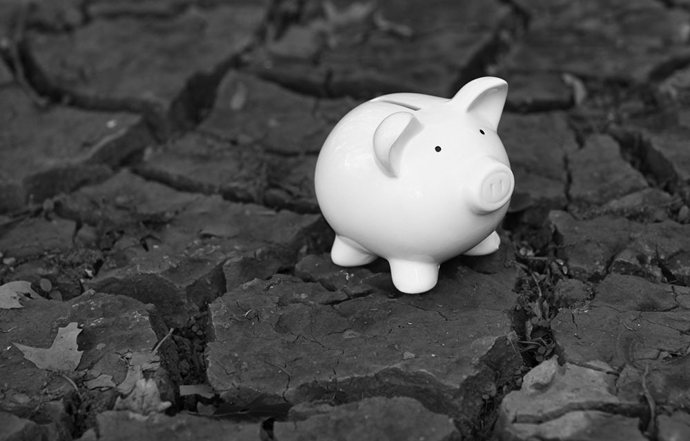 Small, white piggy bank sitting on dry, cracked ground