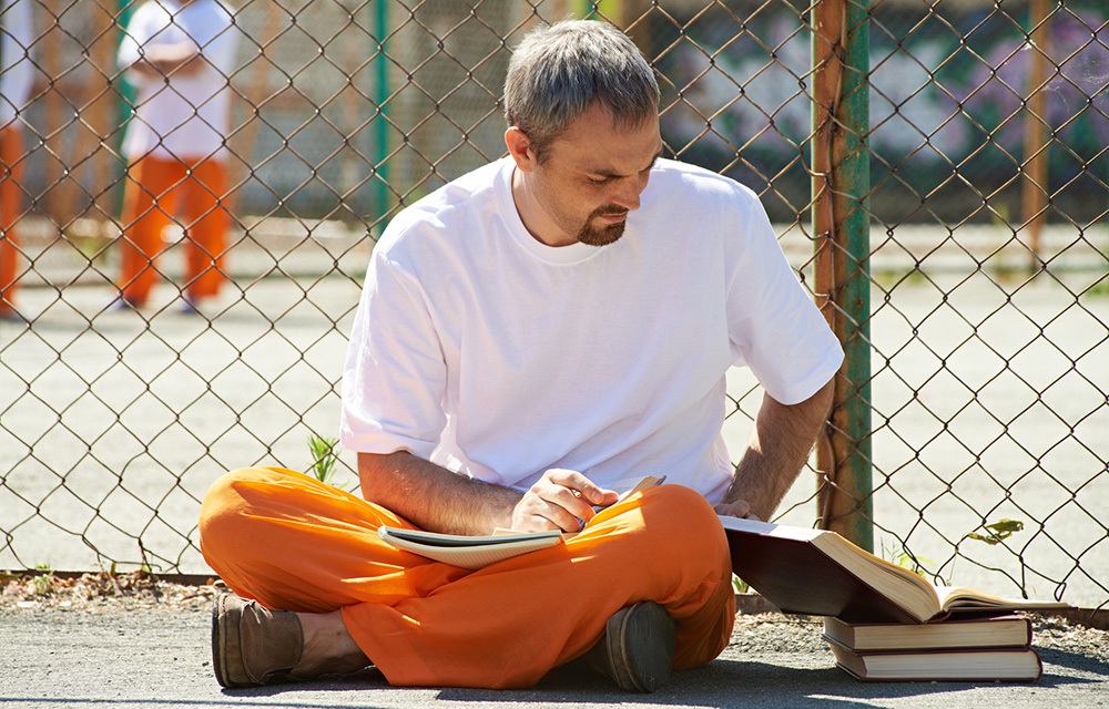 Guy in orange pants sitting beside a fence while looking at books