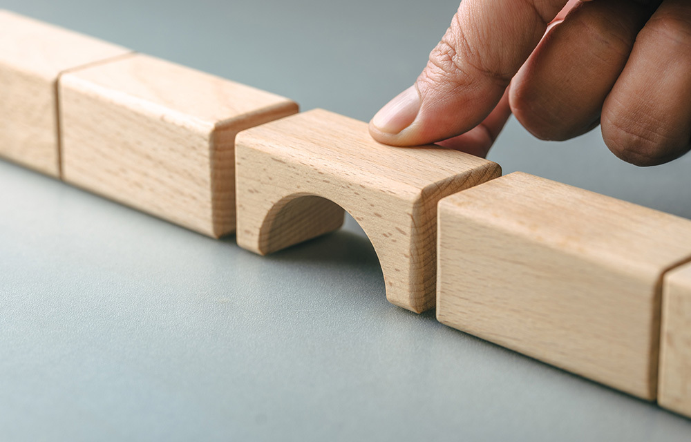 Hand placing a bridge-shaped wooden block to fill a gap in a line of blocks