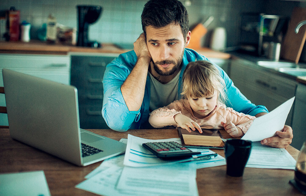 Man staring distressfully at a laptop while holding a baby