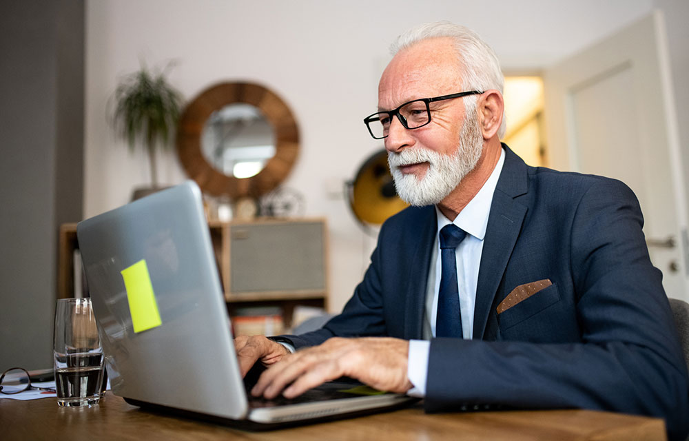 Old bald headed man doing some work on a laptop