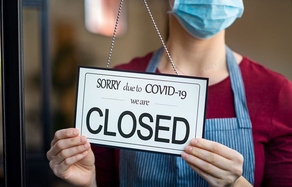 person with mask holding a closed sign