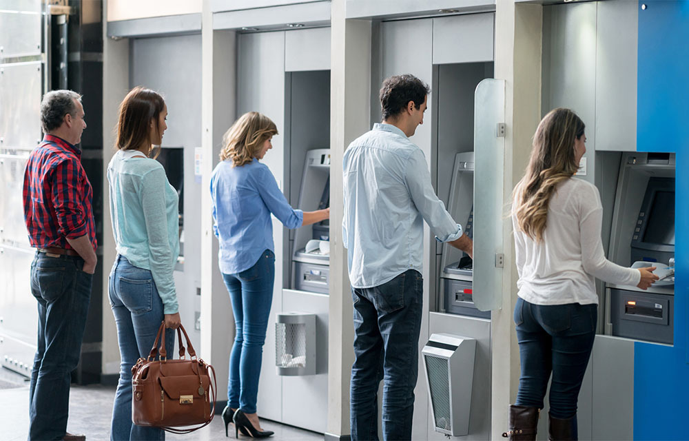 People using an ATM machine with others waiting in line.