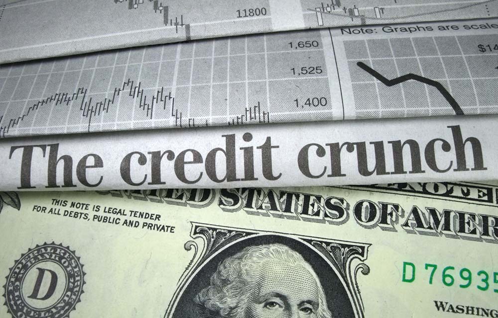 A paper's headline reads "The credit crunch" and is placed on top of a one-dollar bill.