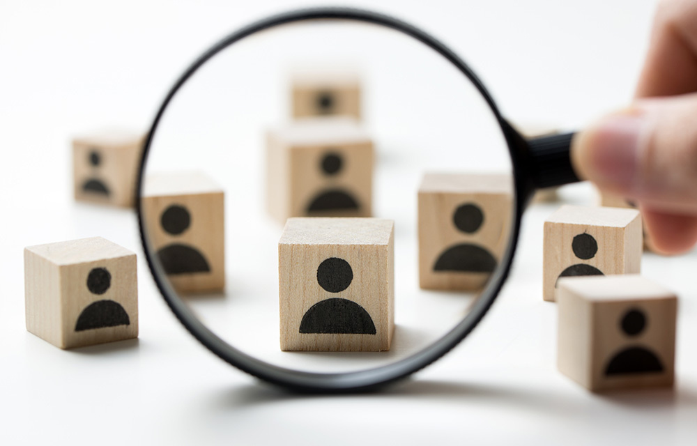 Wooden blocks with a person figure scattered about with a magnifying glass being held in front of one.