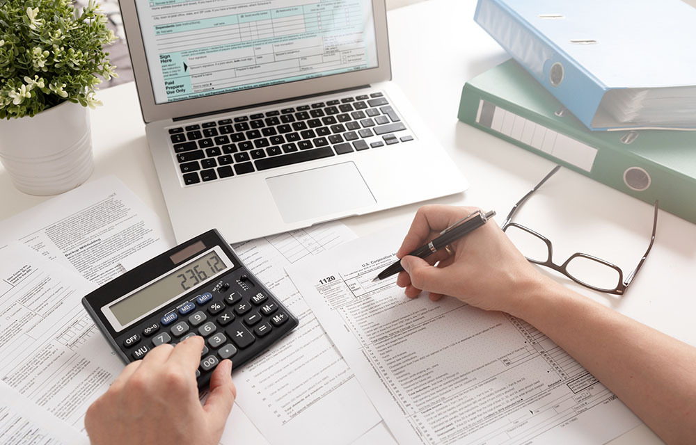 An accountant preparing tax forms for a client on their laptop while using a calculator.