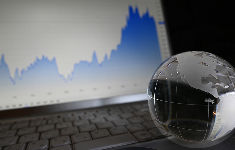 Small glass globe sitting in front of laptop with market charts on screen.