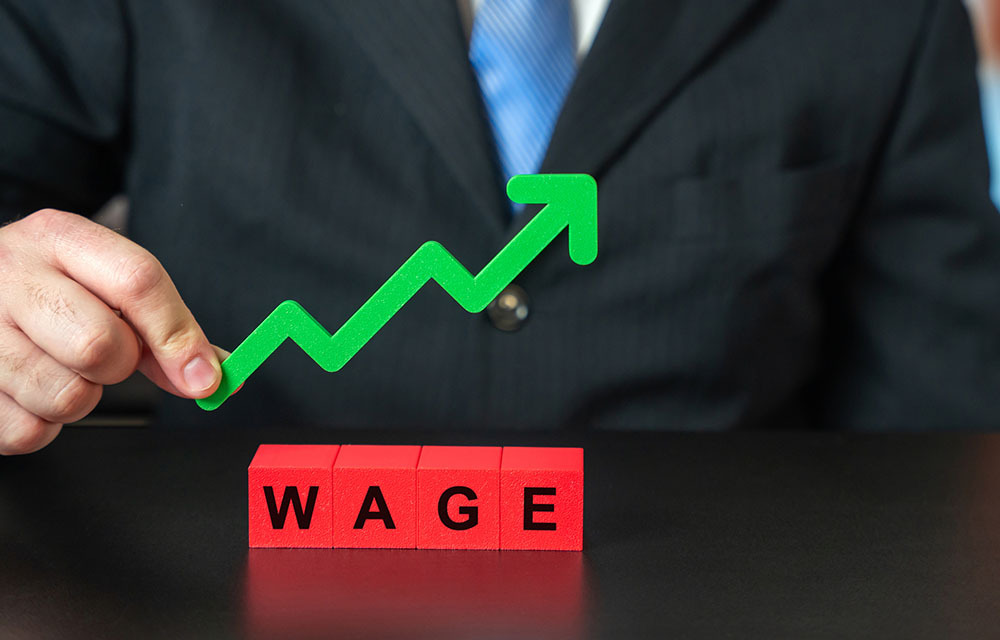 Businessman holding an upward trending label above wooden blocks that spell out "wage."
