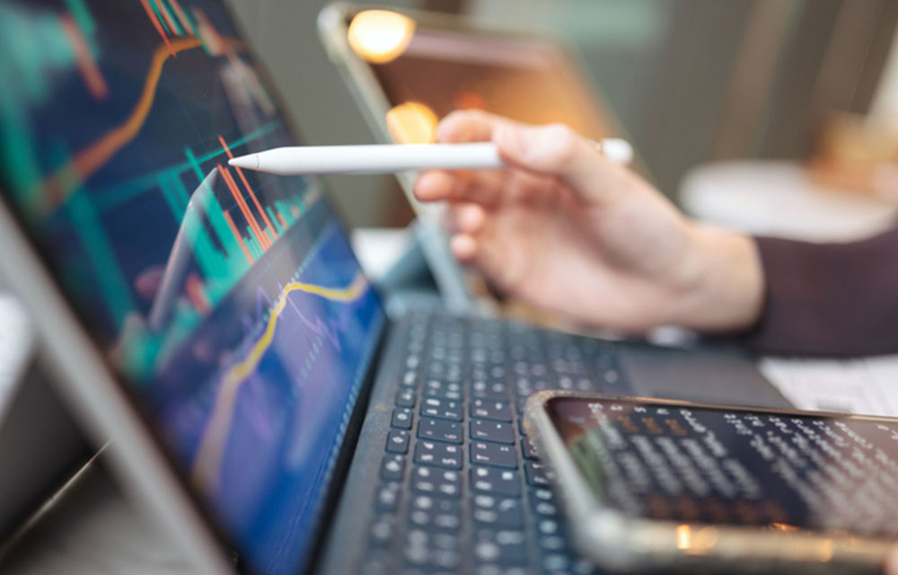 Close-up of a person using a stylus to interact with stock market charts on their laptop.