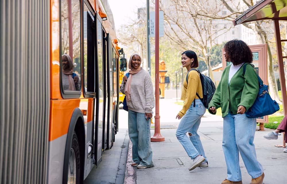 Three college students boarding a bus outside their school.