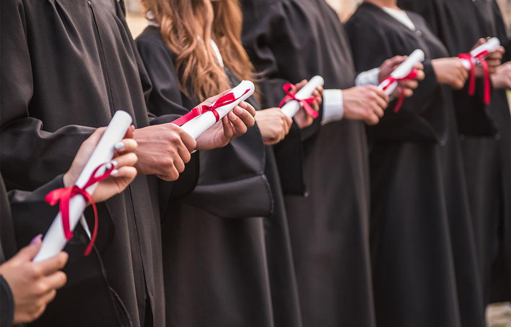 College graduates in black robes holding their diplomas.