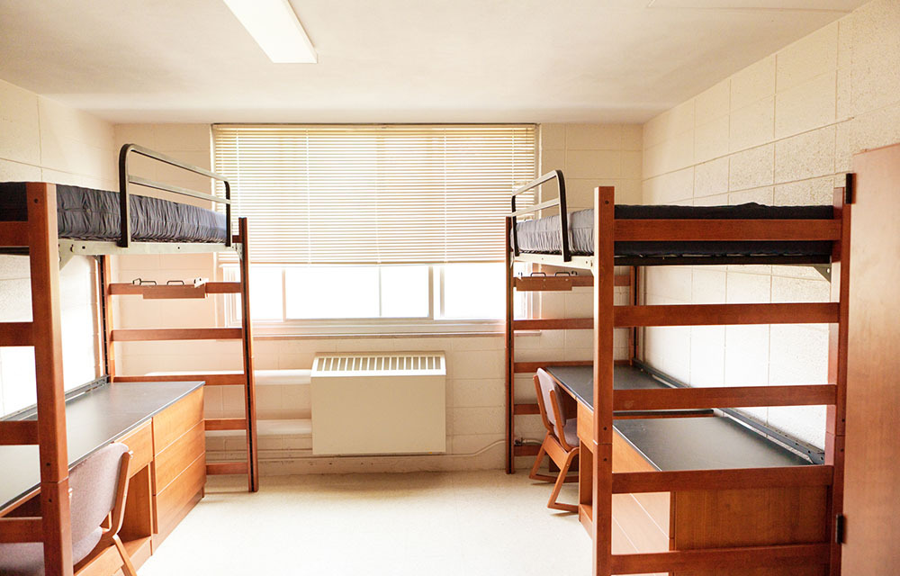 Empty college dorm room with bunk beds and desks.