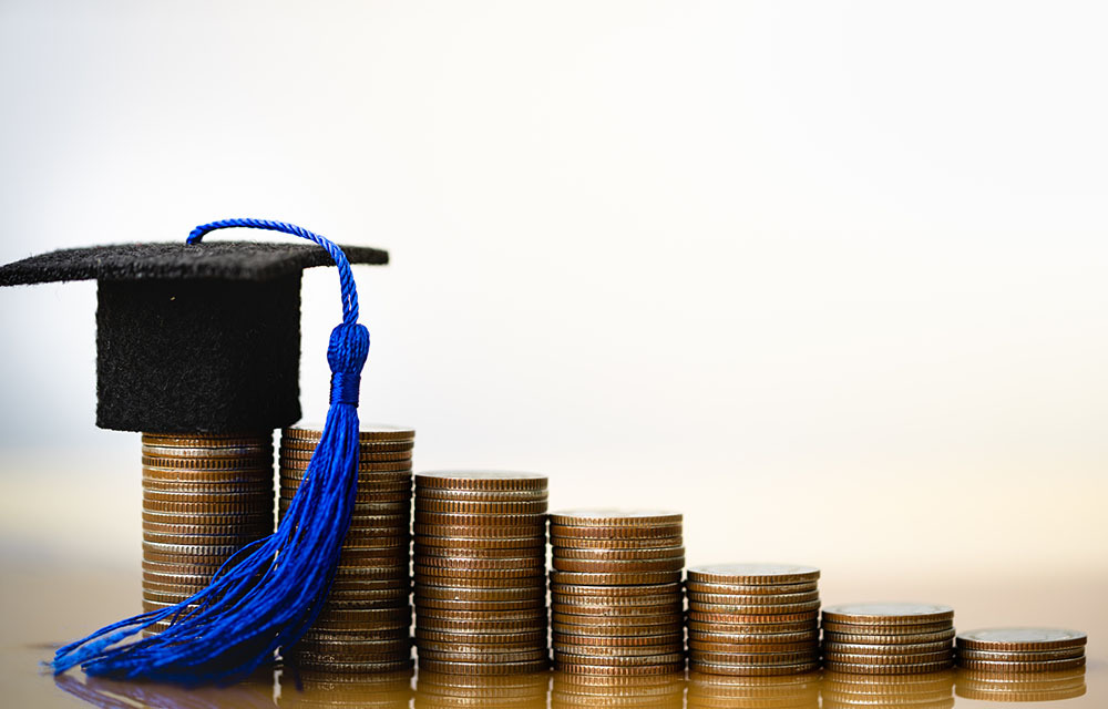 Stacks of quarters with a small graduation hat ornament sitting on top of the largest stack.