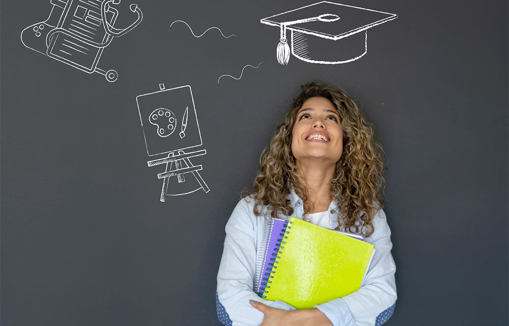 Happy student thinking about what to study as her major and looking at the options on a blackboard while smiling.