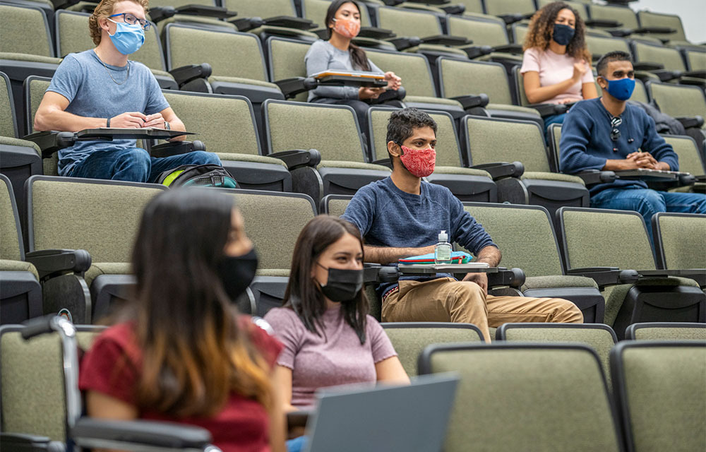College students sitting in lecture hall with masks on during the COVID-19 pandemic.