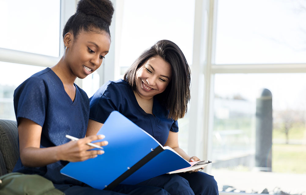 Two nursing students in community college are sitting next to each other to study and share notes.