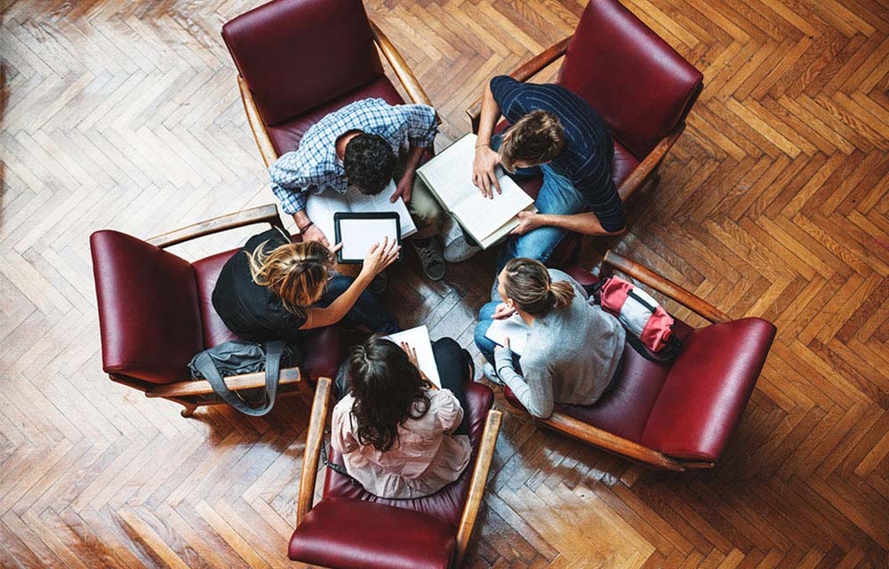 Overhead shot of a group of students studying and comparing notes in a library.