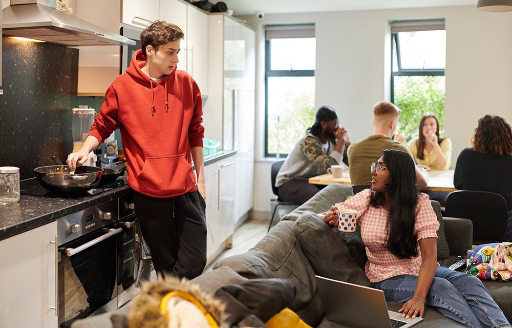 Group of college students relaxing and cooking in a dorm room.