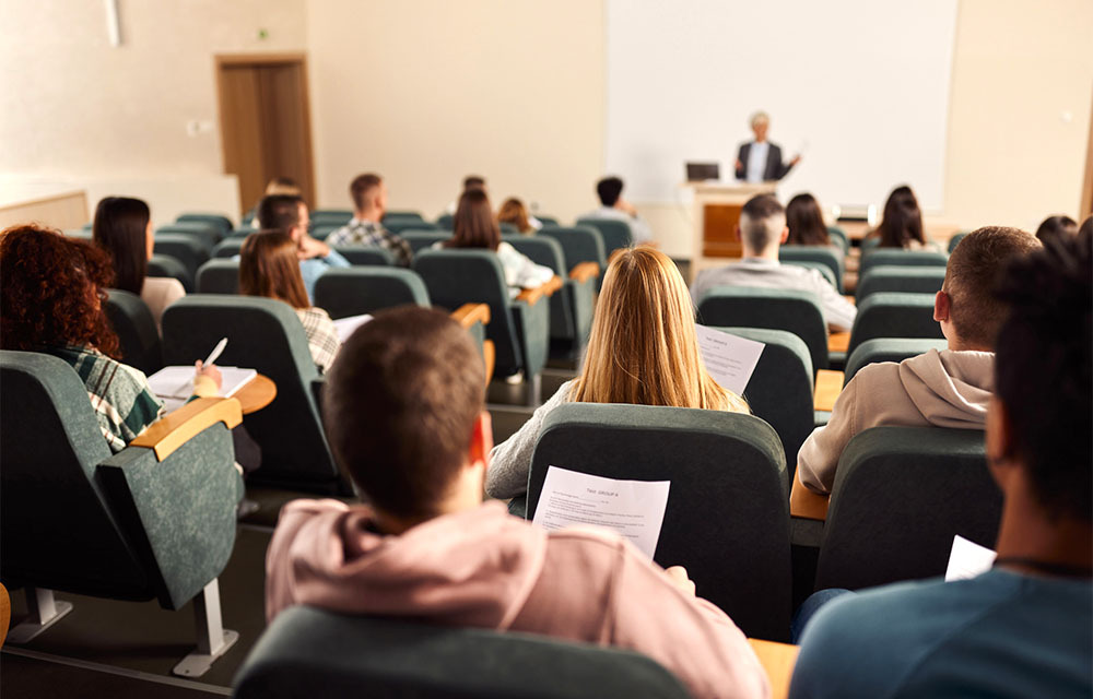 Group of students in a lecture hall highlighting in their books as the professor speaks.