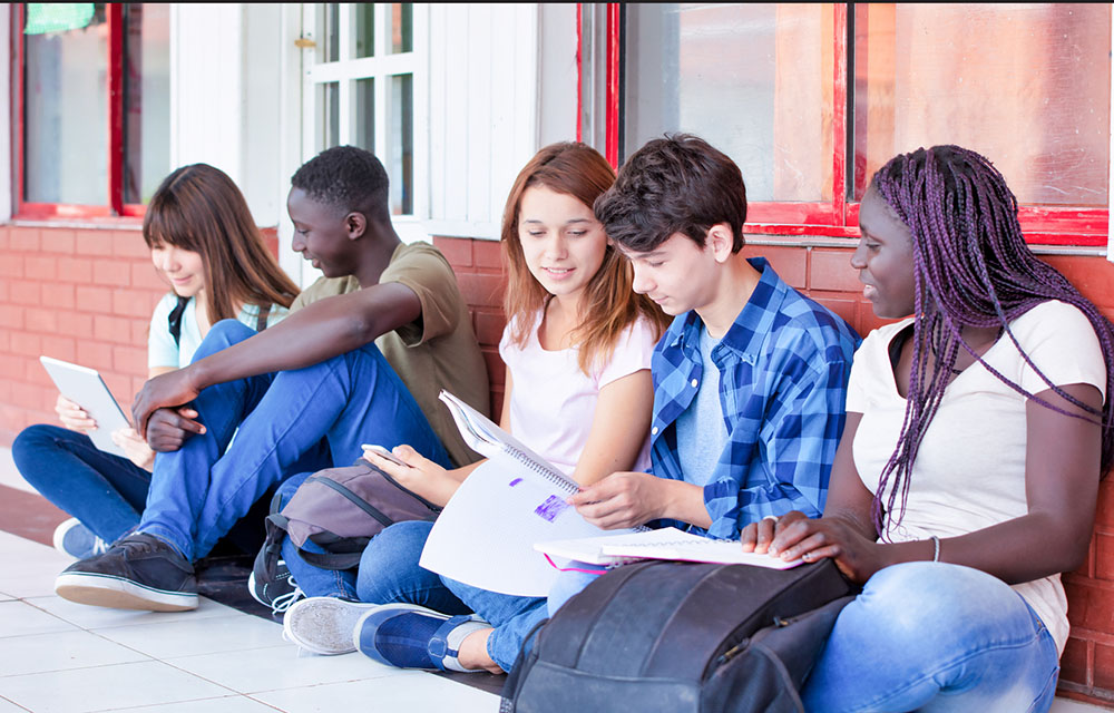 Group of dual enrollment students sitting outside of school studying and looking at notes.