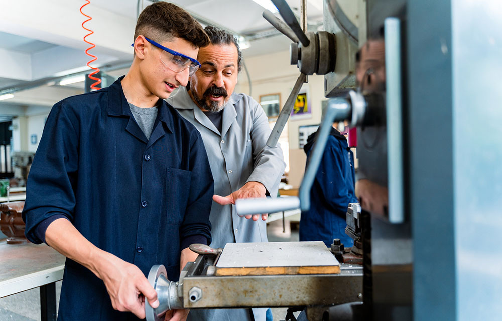 Young man wearing safety goggles and receiving vocational training from his teacher.