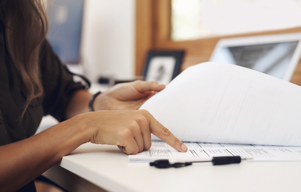 a hand reviewing some documents with a pen in the foreground