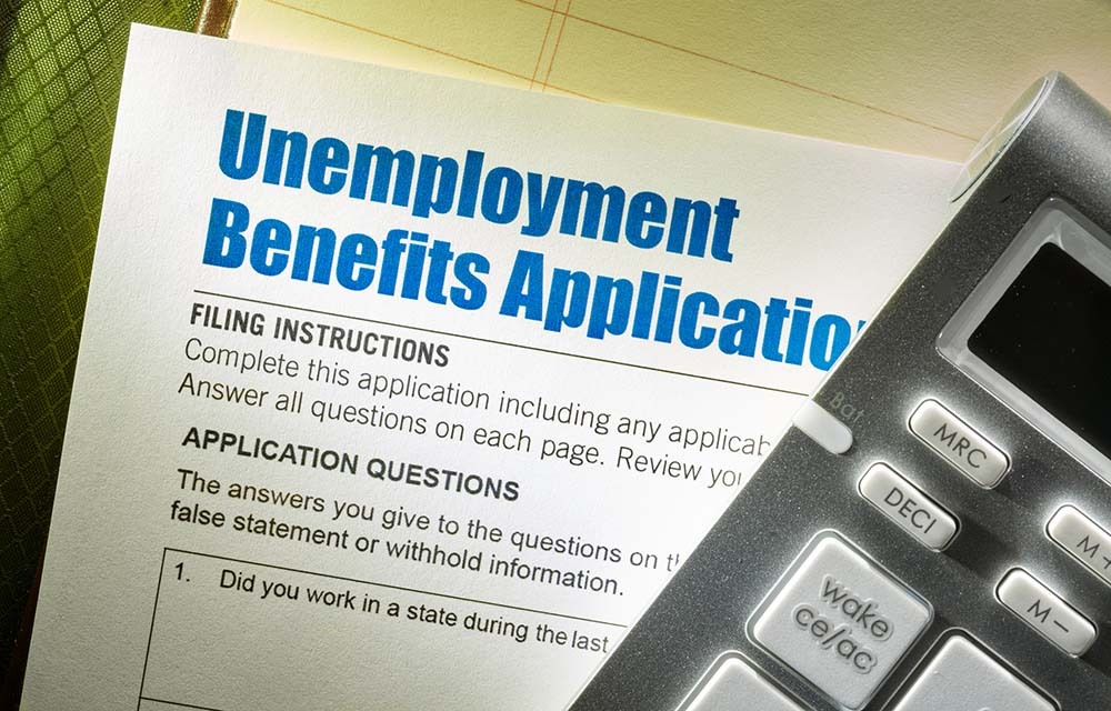 Unemployment Benefits Application and calculator on top of note pad.