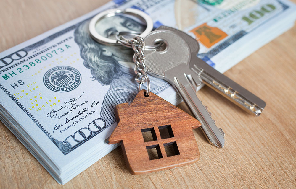 Stack of hundred dollar bills with keychain laying on top of a house.